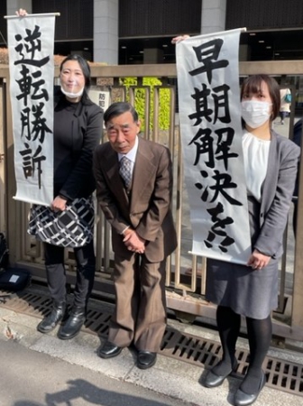 応援にお礼する原告の北三郎さん(中央)。弁護団が「逆転勝訴」「早期解決を」を書かれた紙を掲げている